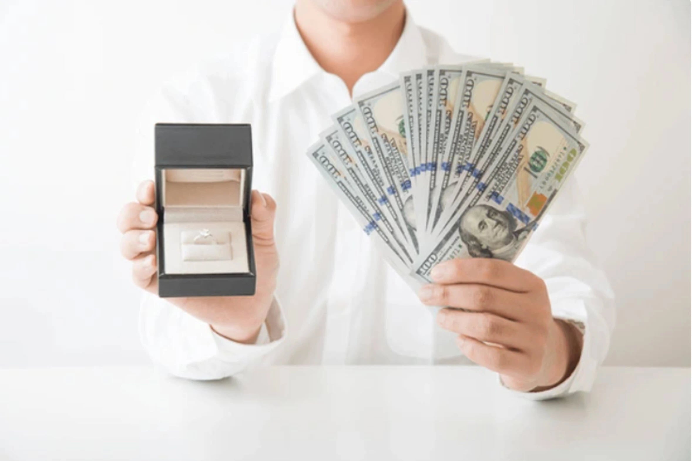 Person holding a ring box and a fan of money on a white background