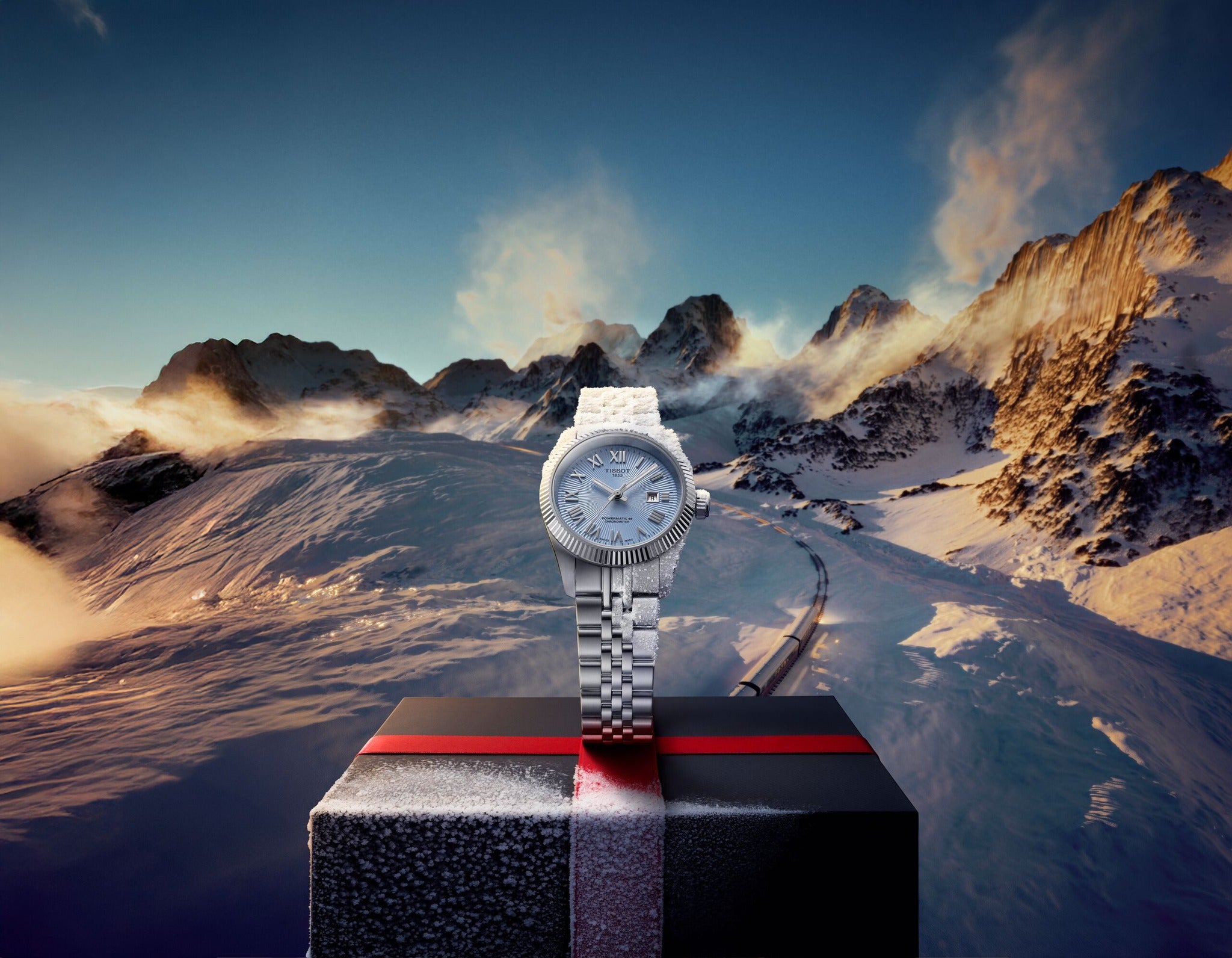 Silver watch on a black stand with a mountainous landscape in the background