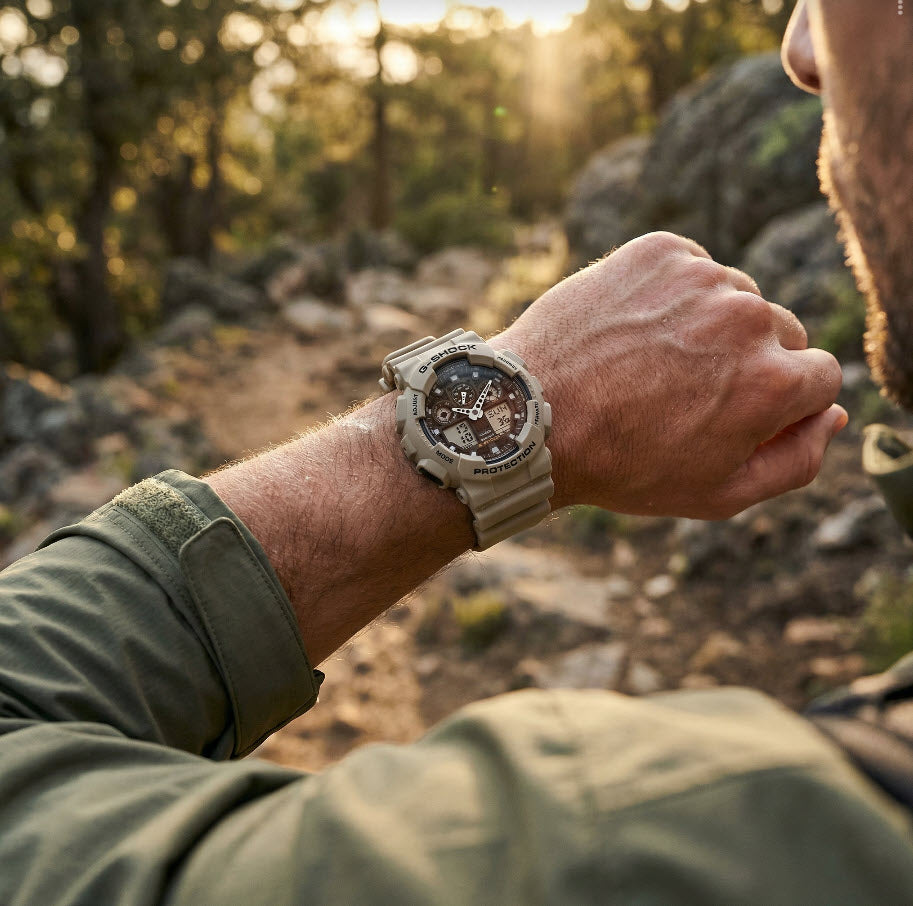 Person wearing a rugged watch in a natural setting with trees and rocks.
