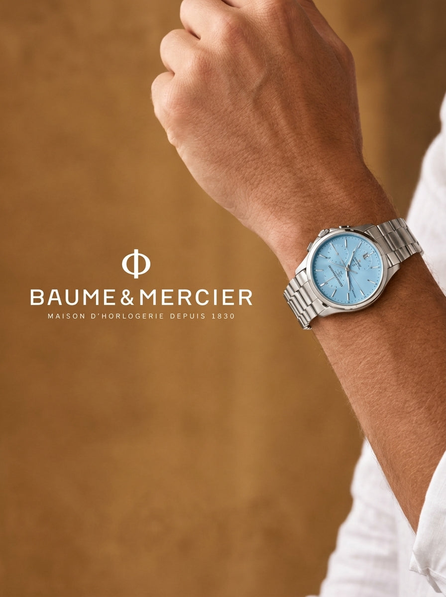 A Baume & Mercier wristwatch with a silver metal bracelet and a light blue dial, worn on a person's wrist. The image features a warm brown textured background and the Baume & Mercier brand logo and name on the left side.