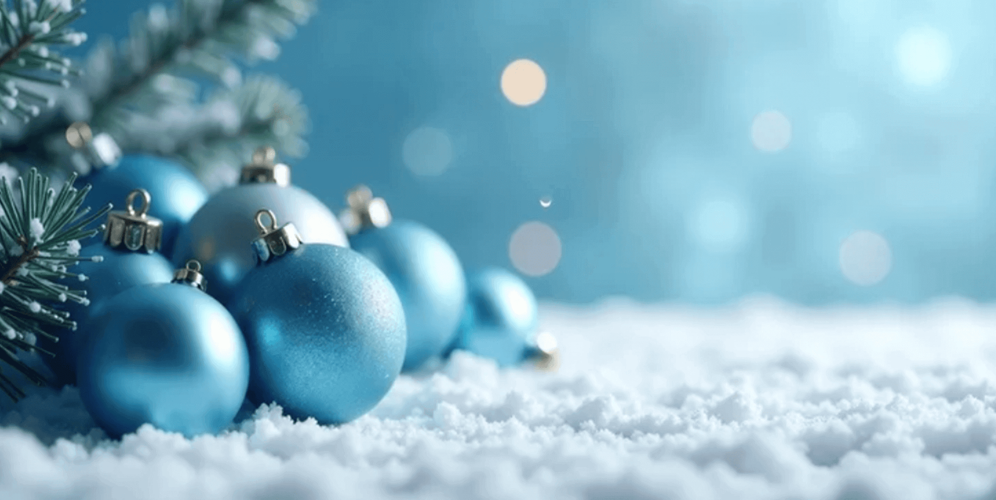 Blue Christmas ornaments on a snowy surface with a blurred light blue background