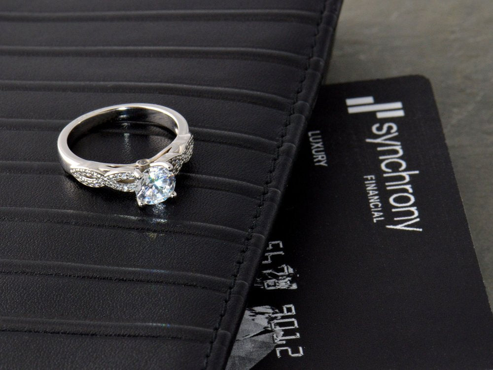 Diamond ring on a black surface with a card displaying 'Synchrony Financial'.
