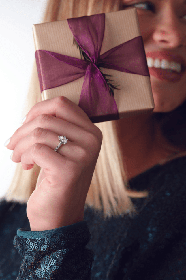 Woman holding a gift box with a purple ribbon, wearing a ring.