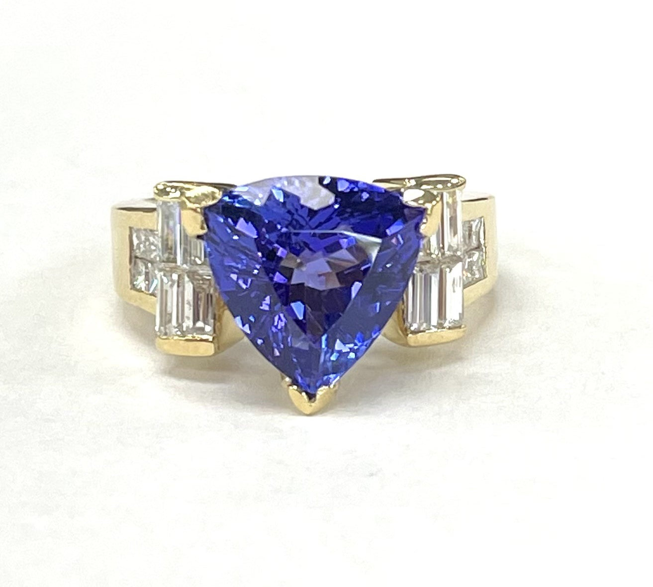 An 18KT yellow gold ring with a 3.07CT trillion tanzanite and diamond inlay, featuring a gold band and a prominent blue tanzanite stone.