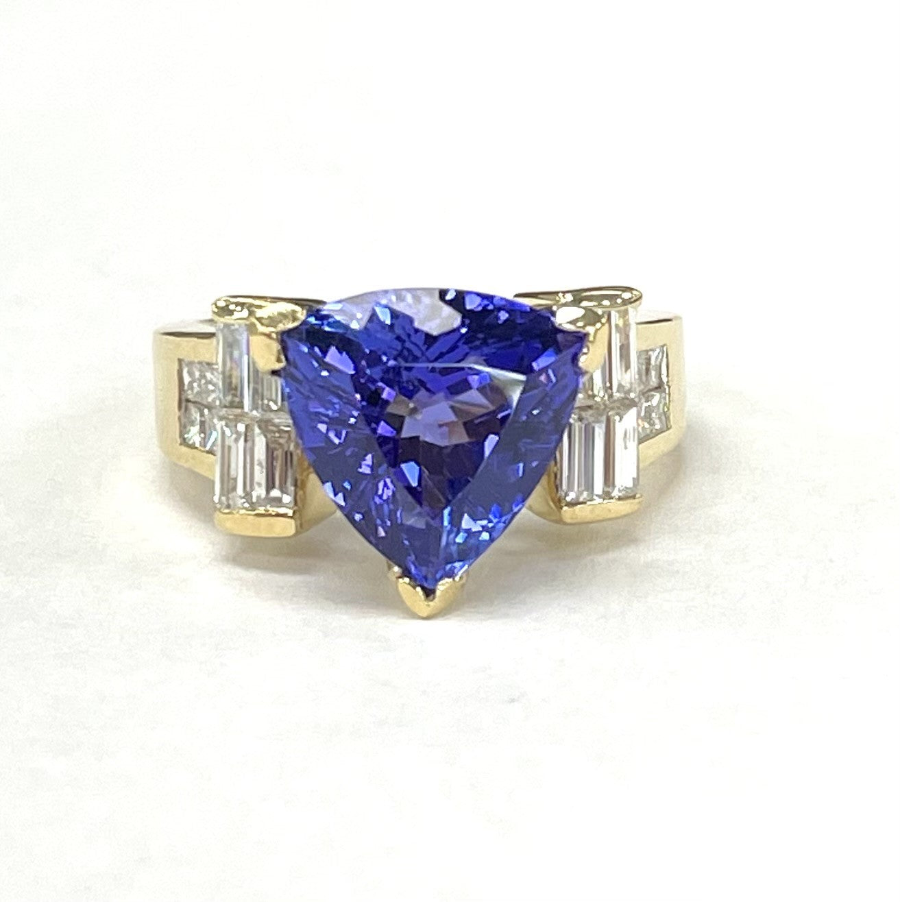 An 18KT yellow gold ring with a 3.07CT trillion tanzanite and diamond inlay, featuring a gold band and a prominent blue tanzanite stone.